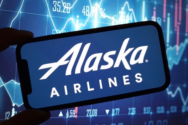 A hand holding a smartphone with the Alaska Airlines logo.